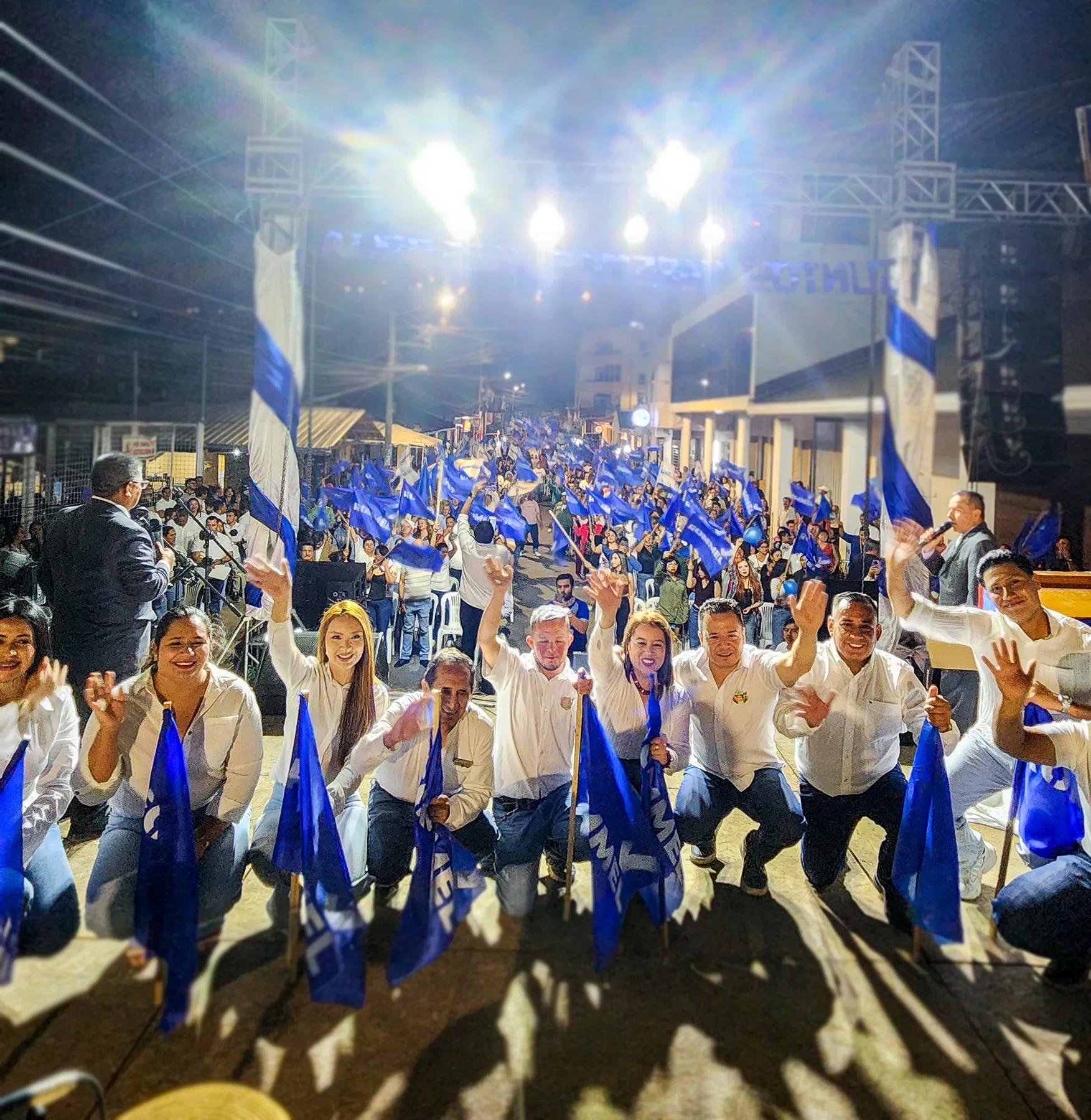 Grupo de participantes saludando entre numerosas banderas azules