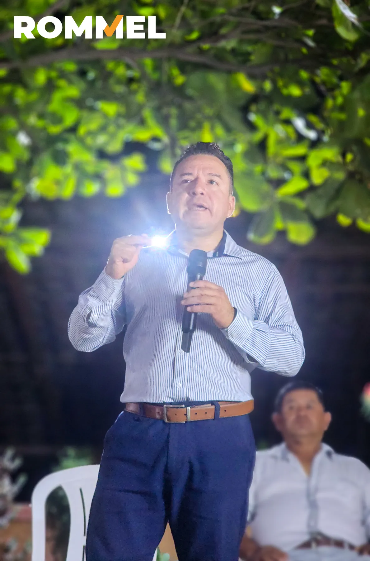 Rommel Durán hablando ante vecinos bajo árboles iluminados
